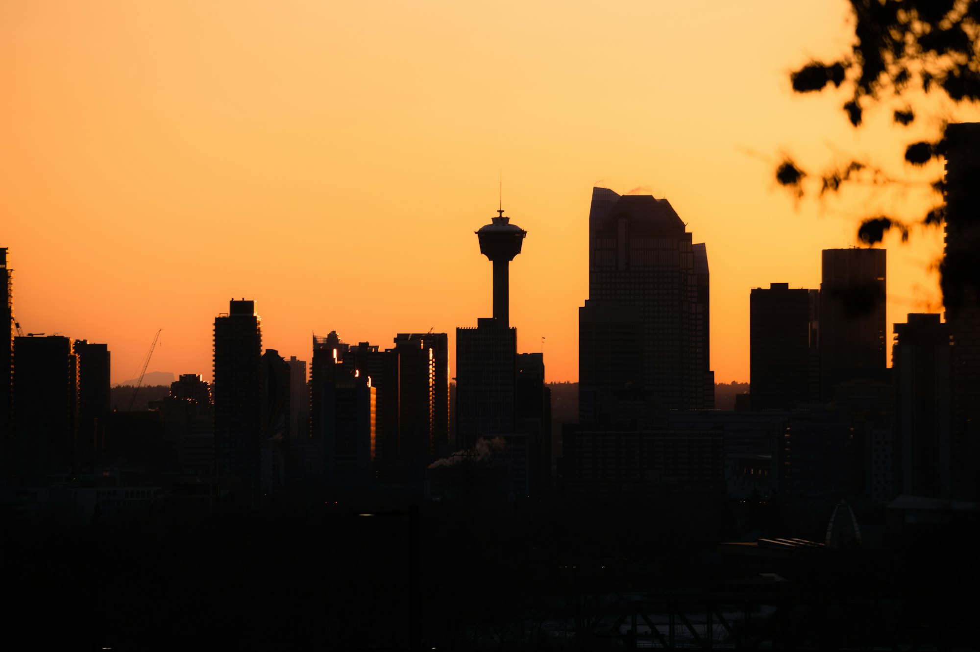 Silhouette of downtown Calgary’s skyline, including the Calgary Tower, against an orange sunset sky.